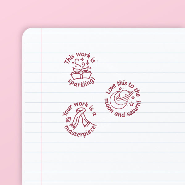 Pop Star Stamp Set 1 - the three teacher marking stamps in the set, stamped in pink ink on lined paper: sparkling, moon and saturn, and masterpiece. My Teacher Says, handmade in Scotland.